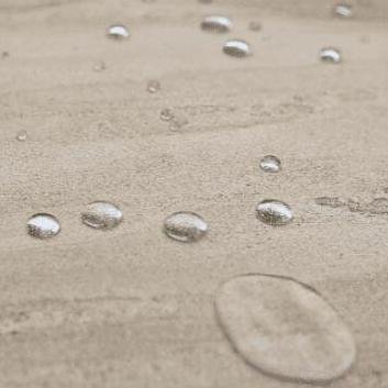 Small, clear water droplets scattered on wet sand with a single oval impression in the foreground.